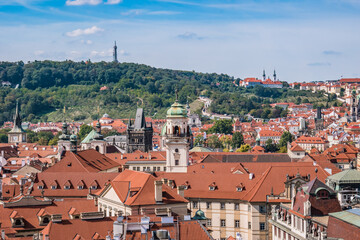Fototapeta na wymiar Roofs and towers of Prague monuments and churches with hill and tower of Petrin in horizon, Czechia