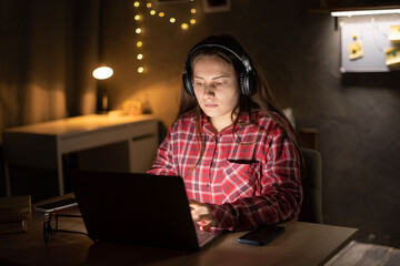 Teenage girl using a laptop and wearing headphones sitting on dormitory. Technology and education