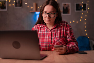 Young woman at home surfing the web, networking and online shopping late at night, she is holding a credit card. Student in dormitory using laptop while payment online purchase.