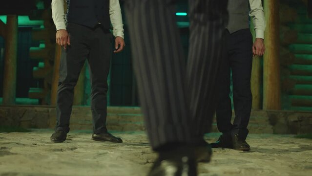 Young man flipping upside down on the floor , doing trick with glass of alcohol drink , drinking . His friends applauding cheering him . Men celebrating , having fun, laughing . Drinking without hands