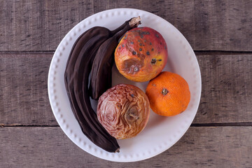 Spoiled fruit on a plate. Bananas, tangerines, apple, orange, top view.