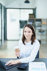 Fototapeta na wymiar A portrait of an Asian businesswoman showing a happy smiling face holding a cup of coffee during a break