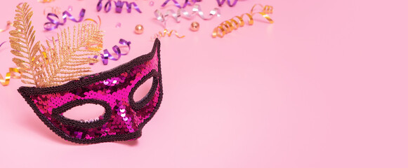 Festive face mask for masquerade or carnival celebration on colored background with tinsel. Banner format