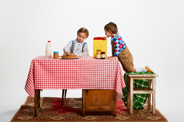 Portrait of two little boys, brothers at table with retro tablecloths cooking dessert, baking. Domestic duties, having fun in the kitchen. Concept of retro style, family, 50s, 60s, fashion, childhood