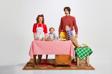 Lovely family. Man and woman standing at kitchen table with two little boys, sons and preparing breakfast, cooking. Relationship. Concept of retro style, family, 50s, 60s, fashion, childhood