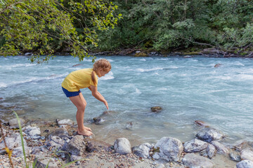 Adorable little child girl playing and having fun near mountain river on warm and sunny summer day. (Holiday, rest, happy childhood concept)