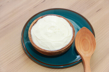 White fermented milk yogurt in a decorative plate, next to a wooden spoon