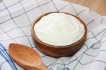 White fermented milk yogurt in a decorative plate, next to a wooden spoon