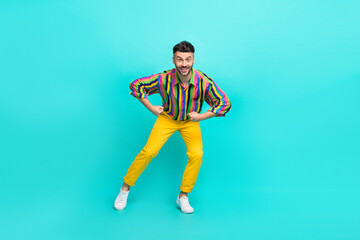 Fototapeta na wymiar Full length photo of positive funky man brunet hair dressed striped shirt yellow pants dancing isolated on turquoise color background