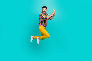 Fototapeta premium Full length size photo of funky jumping youngster guy hold smartphone take shot video call online remote conference isolated on cyan color background