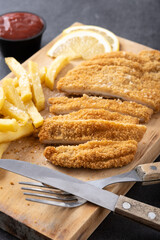 Wiener schnitzel with fried potatoes on black background