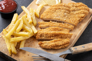 Wiener schnitzel with fried potatoes on black background