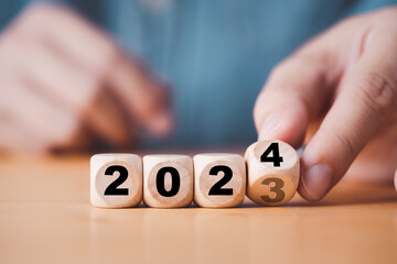 Hand flipping of 2023 to 2024 on wooden block cube for preparation new year change and start new...