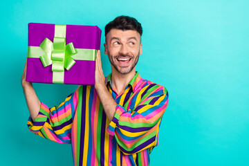 Portrait of handsome impressed guy with brunet haircut wear colorful shirt present box look empty space isolated on teal color background