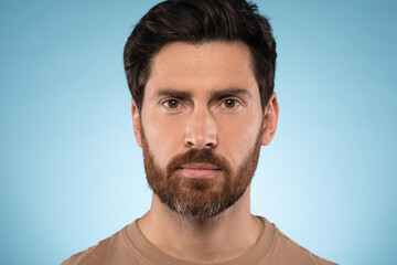 Portrait of handsome bearded man posing and looking at camera, standing over blue studio background, closeup headshot