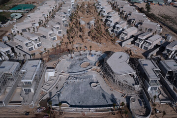 Luxury resort or residential development under construction from aerial view featuring swimming pool and villas in beach or desert location.