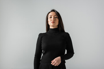 asian businesswoman in black turtleneck looking at camera isolated on grey