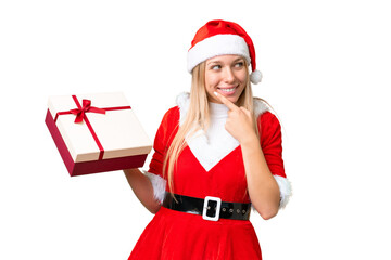 Young blonde woman with christmas hat and holding a gift over isolated chroma key background thinking an idea and looking side