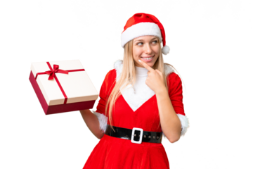 Young blonde woman with christmas hat and holding a gift over isolated chroma key background thinking an idea and looking side