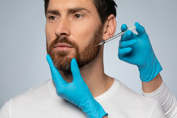 Bearded man getting beauty injection, cosmetologist hands in gloves doing anti-aging procedure for man