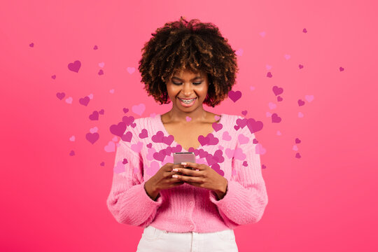 Glad young black curly lady with braces typing on phone with many hearts, reading message - Powered by Adobe