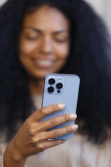 Happy BIPOC woman using blue smart phone with triple camera. Cheerful black female person browsing modern mobile phone