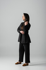 Obraz na płótnie Canvas full length of young asian businesswoman in black suit standing on grey