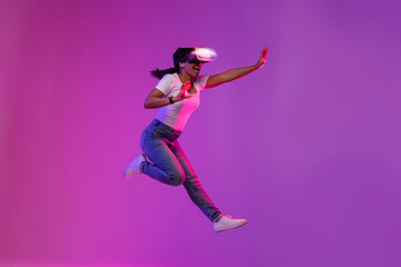 Excited Young Black Female Wearing Glowing VR Glasses Jumping In Neon Light