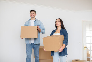 Relocation Concept. Happy Young Spouses Walking With Cardboard Boxes In Hands