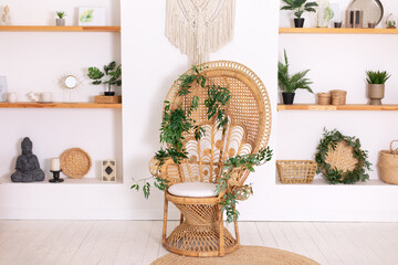Design peacock wicker chair and wooden shelfs with decor in stylish bedroom interior. Rattan peacock armchair by the white wall in the living room. Wabi sabi room interior. Eco natural furniture.	