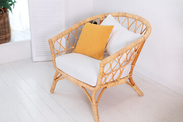 Design wicker wooden chair with pillows in stylish light bedroom interior. Rattan armchair by the white wall in the living room. Wabi sabi room interior. Eco natural furniture. Scandinavian style home
