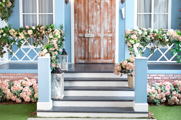 Wooden porch of house with different flowers. Terrace of summer house. Spring design home with bloom flowers and decoration lanterns on steps. House entrance staircase at home decorated for easter.	