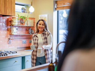 Smiling woman carrying tea for friend in kitchen