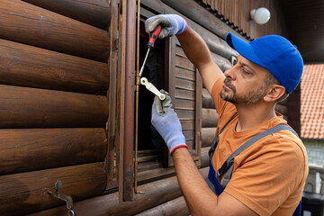 Wooden house maintenance concept. Man holding screwdriver to fix pull handle on wooden shutter.