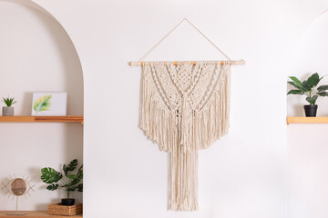 Modern composition of wabi sabi interior with shelf with home decoration and macrame. Stylish interior of living room and wall panel in style of Boho made of cotton threads using macrame technique	