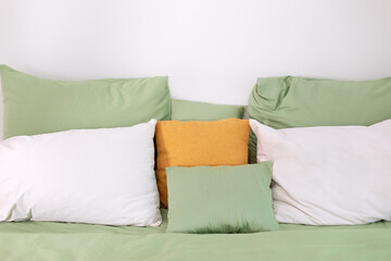 Fototapeta na wymiar Soft different pillows, blanket and duvet cover on bed. Green linens. Bedroom with bedding. Front view. Bed maid-up with clean white pillows and bed sheets. Colorful Pillows on hotel bed