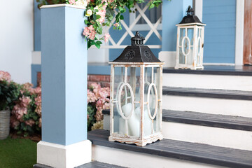 Wooden porch of the house with wooden lanterns. House entrance staircase decorated for spring. Wedding decor in rustic style. Two vintage lamp with candles standing steps outdoor