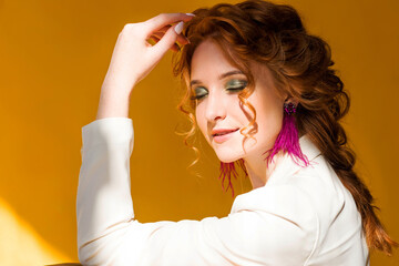 Long purple ostrich feather earrings on a red-haired girl in a white jacket. Girl posing on orange background in sunny weather