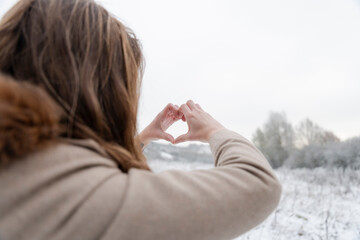 Rear view of woman making hand heart sign in winter landscape