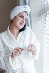 Woman in bathrobe and towel turban talking on smart phone and filing her nails