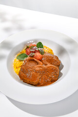 Traditional italian dish - osso buco with risotto milanese. Stew meat on bone with rice on white plate. Summer italian dining. Italian osso buco with garnish with hard shadows