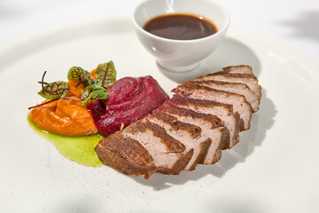 Roast duck fillet with vegetables puree and sauce on light background. Elegant dish from duck fillet and vegetables in summer menu Roasted and sliced duck breast with gravy on white plate