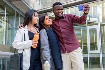 Happy attractive coworkers taking a selfie with a smartphone outside the office. Group of young friends smiling in a work break in the city. Ethnic diversity and social inclusion. Copy space.