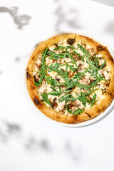 Mushroom pizza with cheese and arugula on white background with shadows. Italian pizza with porcini mushrooms on white table and hard shadows Cheese pizza in trendy style. Modern italian food