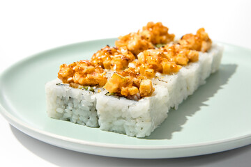 Sushi topped burnt shrimp tartare. Maki sushi with shrimp and spicy sauce on ceramic plate Baked maki roll topped shrimp tartare isolated on white background with hard shadow