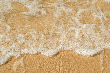 Transparent wave with white foam over the golden sand. Crystal clear sandy beach. Background with eco friendly place for rest.