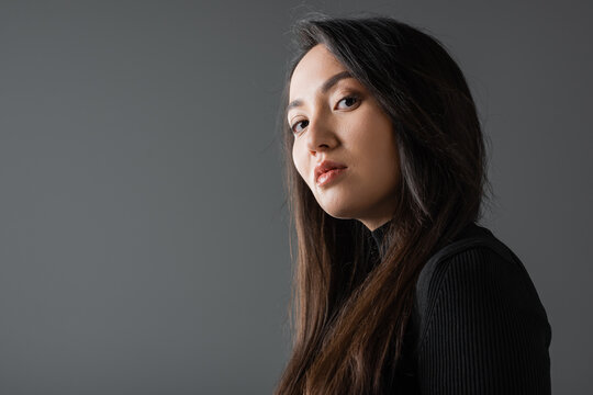portrait of asian woman in black turtleneck looking at camera isolated on dark grey