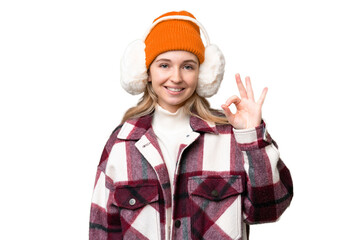 Young  English woman wearing winter muffs over isolated background showing ok sign with fingers