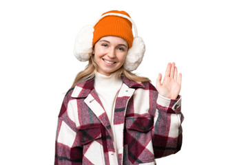 Young  English woman wearing winter muffs over isolated background saluting with hand with happy expression