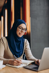 Young nuslim woman working online on computer in a cafe